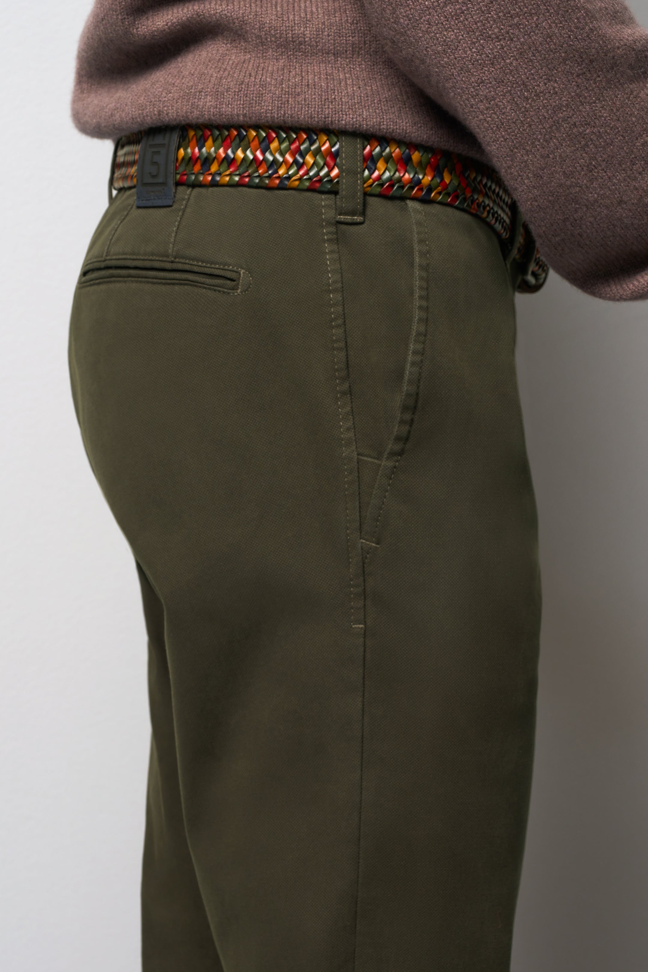 Person wearing olive green pants with a colorful belt on a plain background